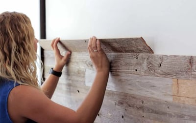 Blonde woman in blue shirt adhering wooden floor panels to white wall - 4 Elegant Half Wall Wood Panelling Ideas 