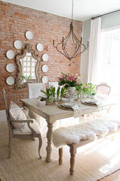 french farmhouse dining room with exposed brick wall, chandelier and light wood dining table