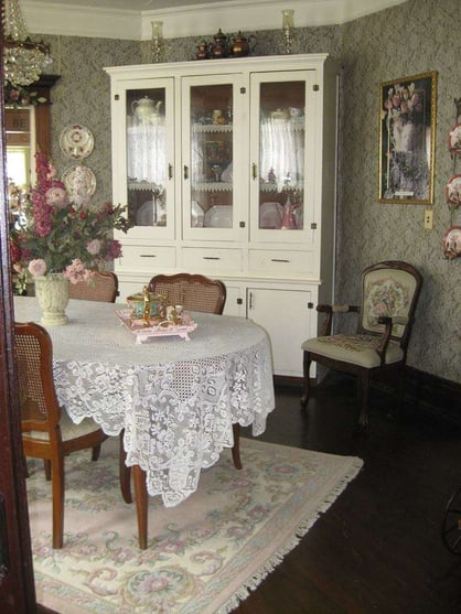 white and pink dining room with lacy table cloth, dark wood dining table and flower patterned wallpaper 