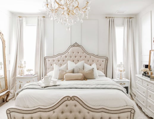 white french-inspired bedroom with upholstered headboard and footboard and gold chandelier