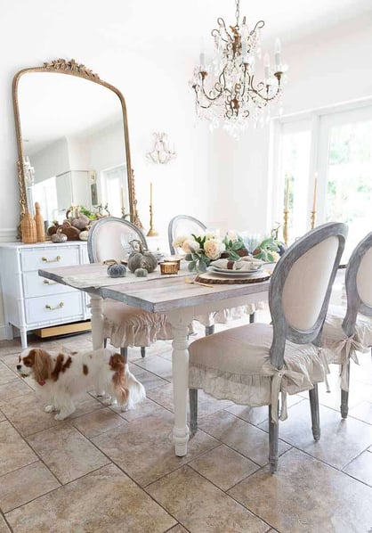 hite french themed dining room with distressed wood dining table in the centre and antique mirror on the wall