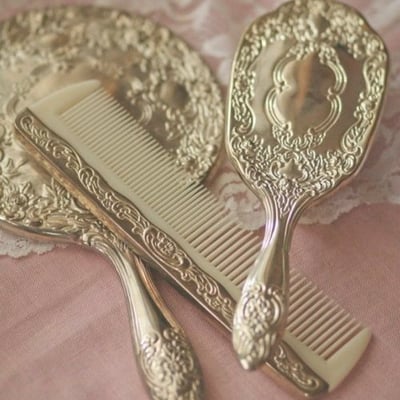 gold ornate vanity set of hand mirror, comb and brush on pink surface